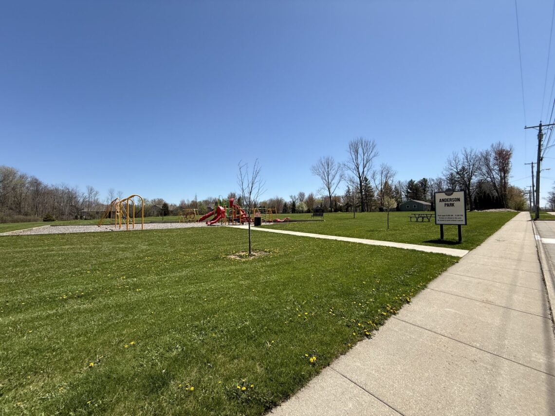 Wide-angle view of Anderson park with a sign and red and yellow playground equipment