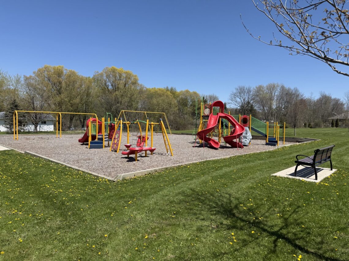 picture of a playground with red and yellow equipment and a bench on the right side.