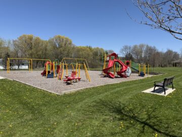 picture of a playground with red and yellow equipment and a bench on the right side.