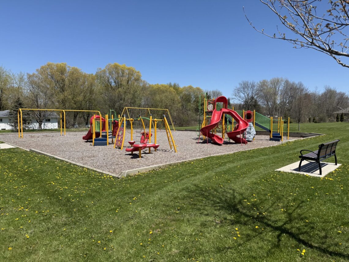 picture of a playground with red and yellow equipment and a bench on the right side.