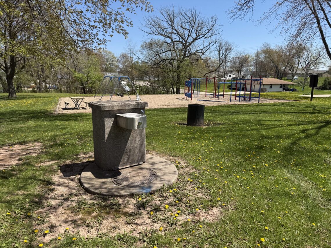 Picture of a drinking fountain with blue and red equipment in the background