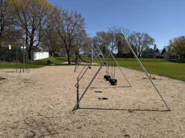 Picture of swing set with climbing equipment and a small slide and benches in the shade