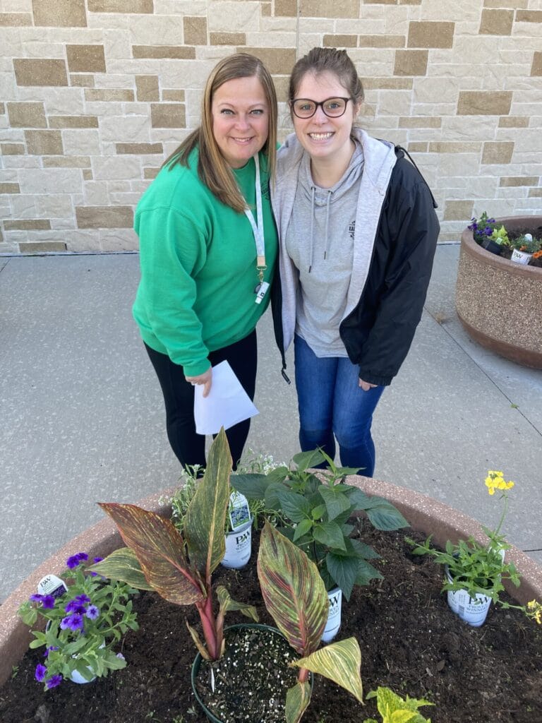 Administrative coordinator Megan Brouch and Marketing and Communications Manager Andrea Fencl plant flowers in pots outside Police Department as part of annual beautification project.