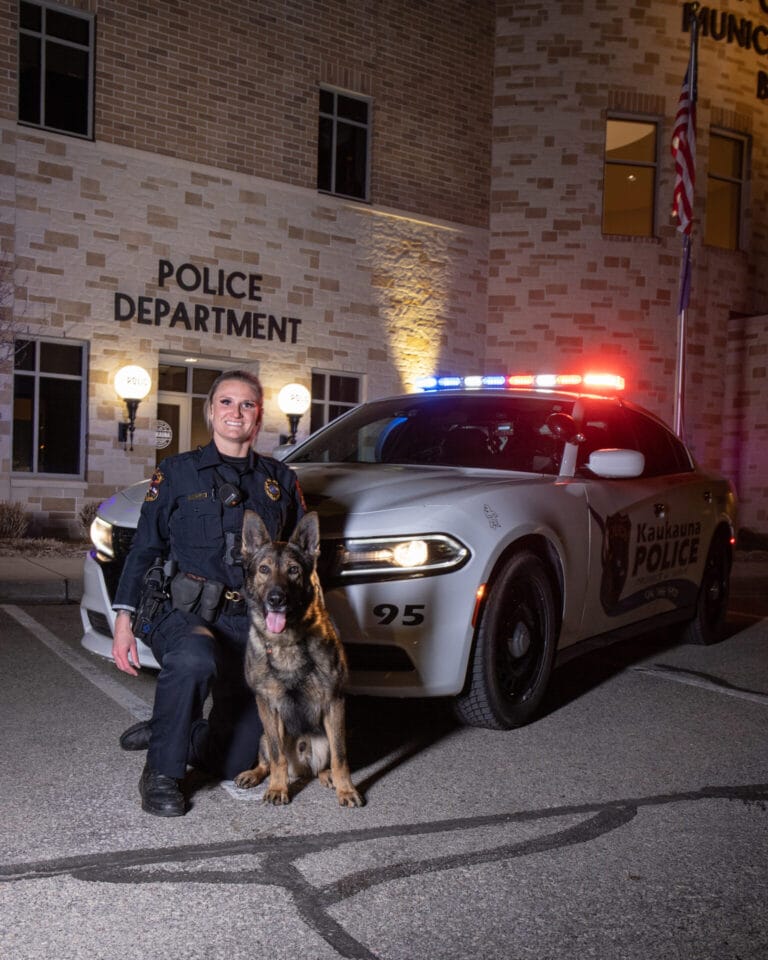 Officer Maas stands in front of the K9 unit vehicle with Bodo