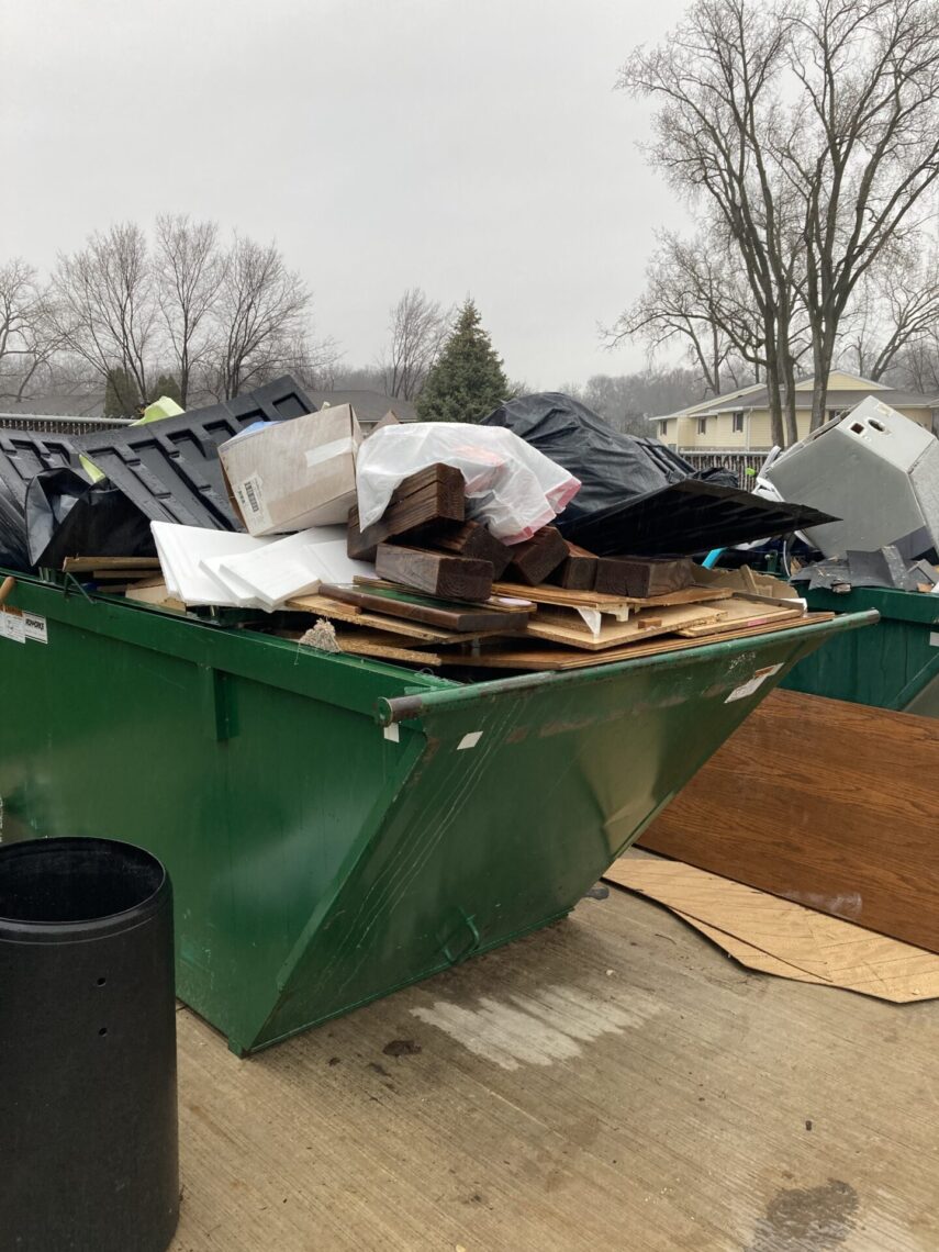 Picture of a green dumpster overflowing with building materials