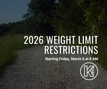 A gravel path stretches through a lush green forest under a clear sky. Overlaid text reads: 